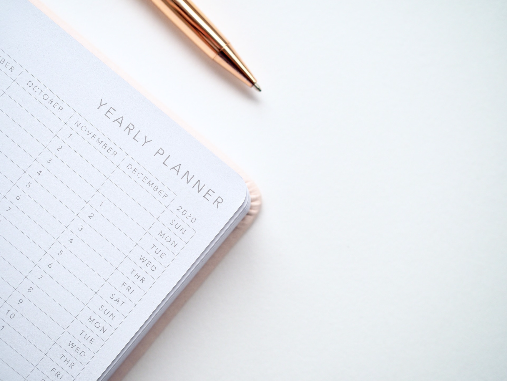A rose gold pen resting on the corner of an open yearly planner.